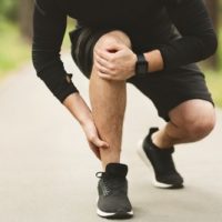 Young male runner is suffering from ankle pain on jogging, free space